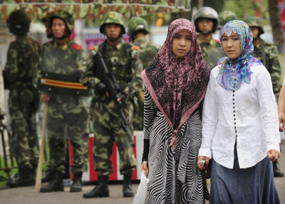 Two ethnic Uighur women pass Chinese paramilitary policemen standing guard outside the Grand Bazaar in the Uighur district of the city of Urumqi