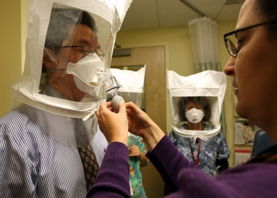 A hospital worker sprays a chemical mist into a protective hood as she fits a doctor