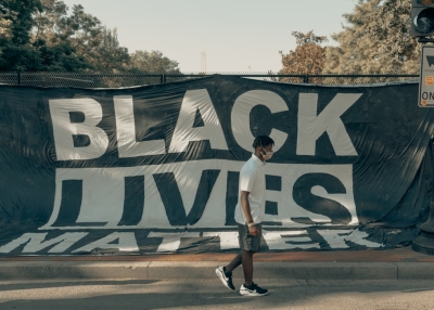 Man walks in front of a Black Lives Matter flag