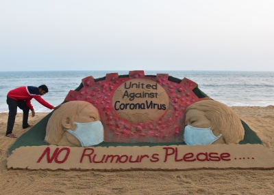 Indian artist Sudarsan Pattnaik puts some final touches as he makes a sand sculpture depicting people wearing protective facemasks with a message reading 'United against corona virus' in Puri