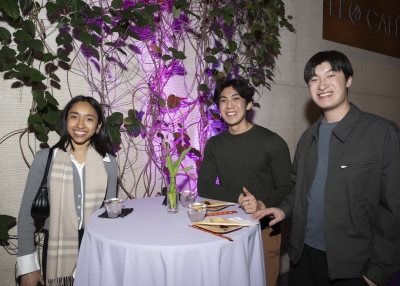 Three individuals stand in front of a vine wall