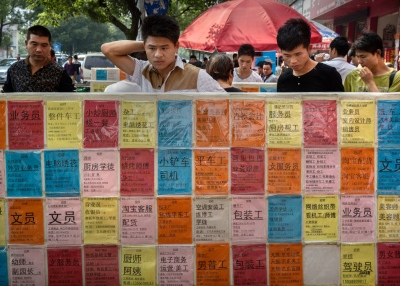 Chinese men look at bulletin boards showing potential jobs outside a job center