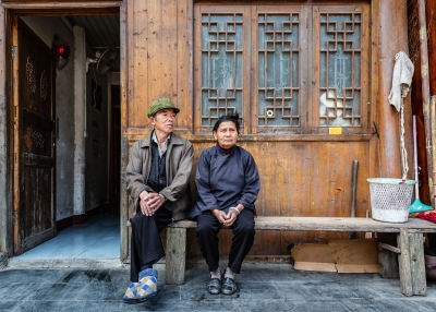 Chinese senior couple sitting side by side on a bench in front of their home in a rural chinese village. 