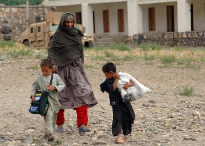 An Afghan woman walks home with her children carrying humanitarian goods after being seen by doctors with the Bagram Provincial Reconstruction Team during a medical civic action program in the district of Tagab in the Kapisa province of Afghanistan April 30, 2007. (Department of Defense)