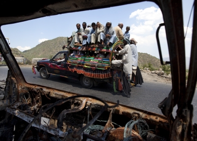 A car packed with people returning to their villages drives by a burned vehicle in Buner, Pakistan on June 23, 2009.