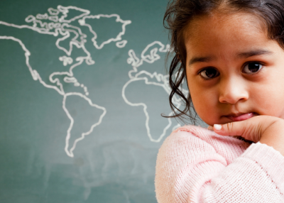 A child sits in front of a chalkboard map of the world.
