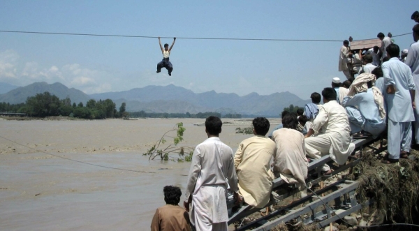 Onlookers perched on a damaged bridge watch a flood survivor  cross a river by rope in the Swat Valley&apos;s Chakdara on August 3, 2010. (STRDEL/AFP/Getty Images)