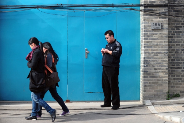 Pedestrians walk past a plainclothes policeman (R) standing in front of the entrance to the studio of outspoken Chinese artist Ai Weiwei in Beijing on April 8, 2011. (Frederic J. Brown/AFP/Getty Images)