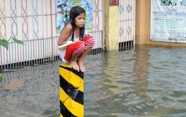 A soaking wet child sits on a post on a flooded street in suburban Manila on August 8, 2012. (Jay Directo/AFP/GettyImages)