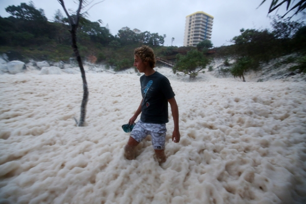 A man walks through ocean foam in Snapper Rocks as Queensland experiences severe rains and flooding from Tropical Cyclone Oswald in Gold Coast, Australia on January 28, 2013. (Chris Hyde/Getty Images)