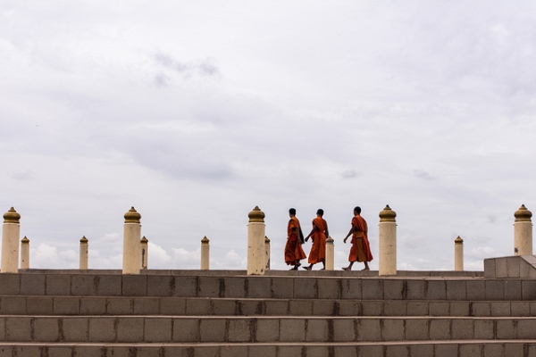 Three monks hurry across the stone steps under a cloudy sky in Vientiane, Laos on June 20, 2013. (Samuel Chan/Flickr)