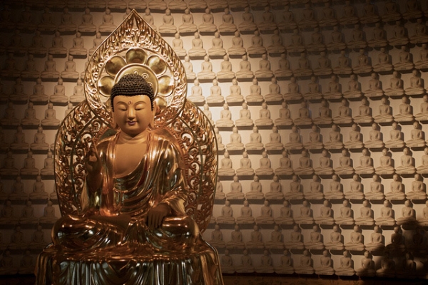 A golden Buddha statue shrouded in light sits surrounded by miniature white Buddha figurines in Seoul Korea on September 2, 2013. (ecodallaluna/Flickr)