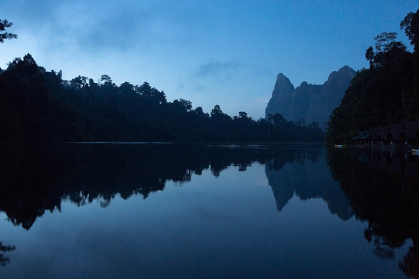Houses, trees and mountains cast shadows on still waters in Khao Sok, Thailand on November 3, 2013. (Stefan Magdalinski/Flickr)