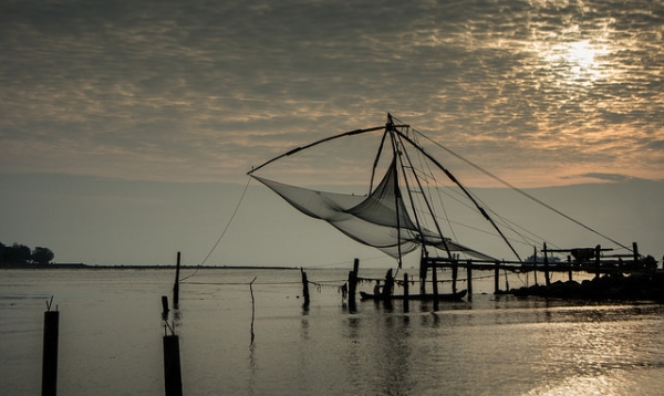 A man rows his boat beneath an empty fishing net hung in the air from some poles in Kerala, India on December 5, 2014. (L0bit0/Flickr)