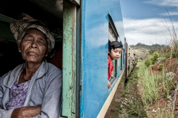 A girl looks out the window of a slow-moving train en route from Loikow to Yangon, Myanmar, as an old woman sleeps. Photograph by Jorge Fernandez. (Smithsonian.com)