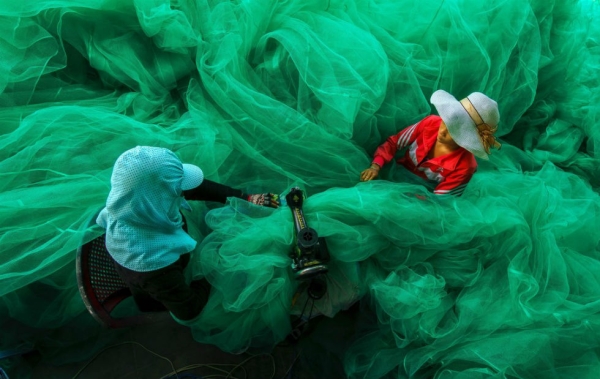 Women of a small village near Vinh Hy Bay, Vietnam, sew a fishing net while their husbands fish. Photograph by Pham Ty. (Smithsonian.com)