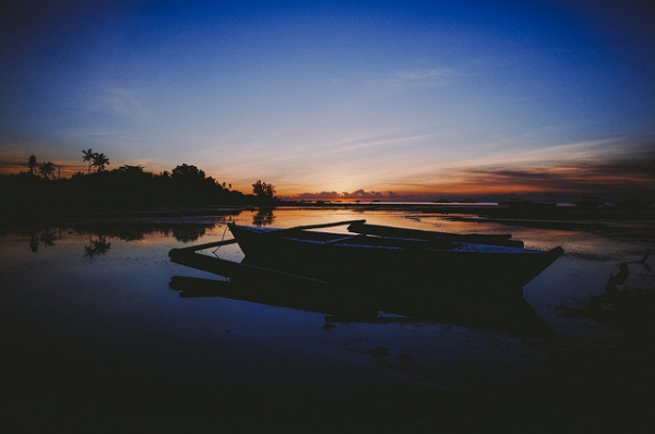 A lone boat rests peacefully on still water against the setting sun in Bohol, Philippines on March 10, 2015. (Ilya/Flickr)