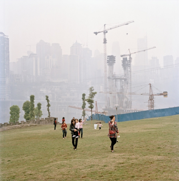 Construction cranes rise in the background mist as women walk with their children across the new grass of a development in Jiangbei. The city’s central business district is in the background. (Tim Franco)
