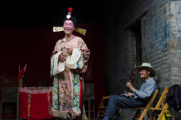 A man in costume smiles at the camera as his friend holding an erhu, a Chinese violin, looks on in Guangxi, China on April 26, 2015. (cotaro70s/Flickr)