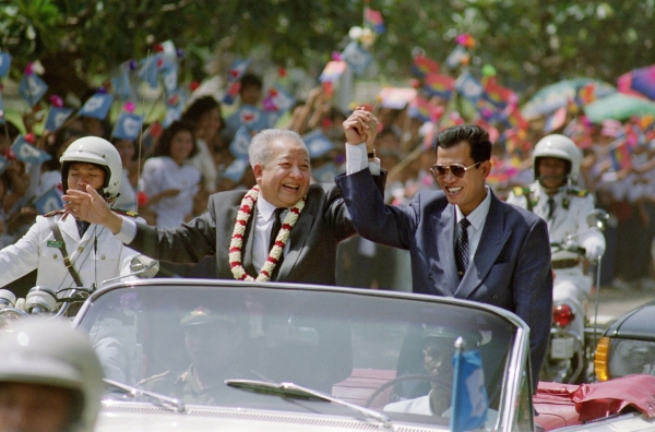 Sihanouk (C) and Cambodian Prime Minister Hun Sen (R), leader of the formerly communist Cambodian People's Party, clasp hands in a motorcade from the Phnom Penh airport following the Prince's arrival in November 1991, after 13 years in exile. (Dominique Faget/AFP/Getty Images)