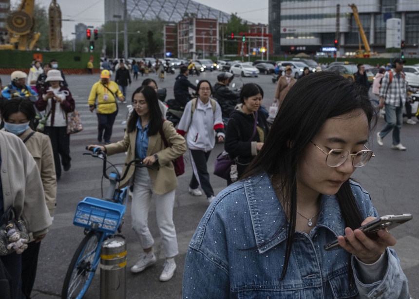  People cross at a traffic light as a screen shows an ad for Apple’s iPhone 16, in Beijing, April 8, 2025. China announced plans Friday to impose a 34 percent tariff on imports of all U.S. products starting April 10, in retaliation following U.S. President Donald Trump’s “Liberation Day” tariff announcement.