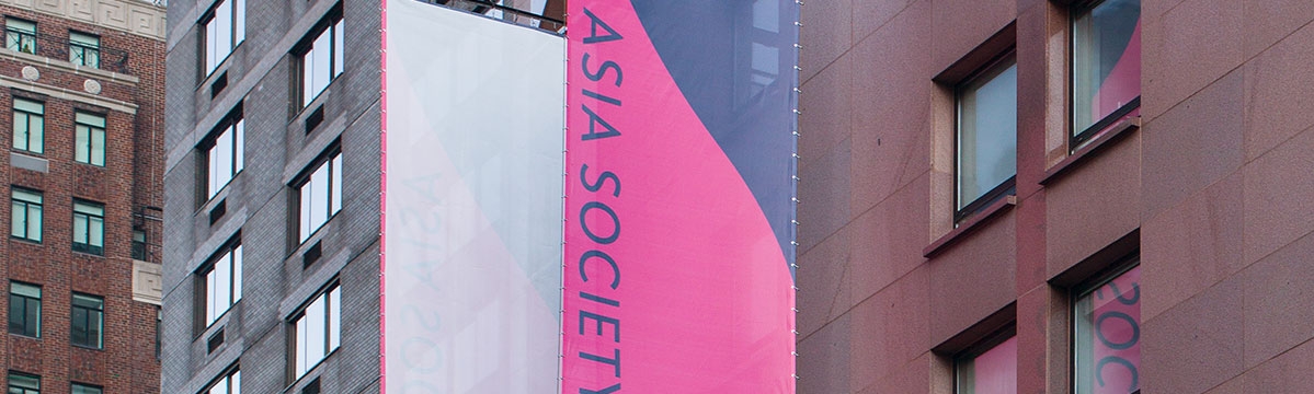 The facade of Asia Society Museum featuring a pink and blue banner reading "Asia Society Triennial: We Do Not Dream Alone"