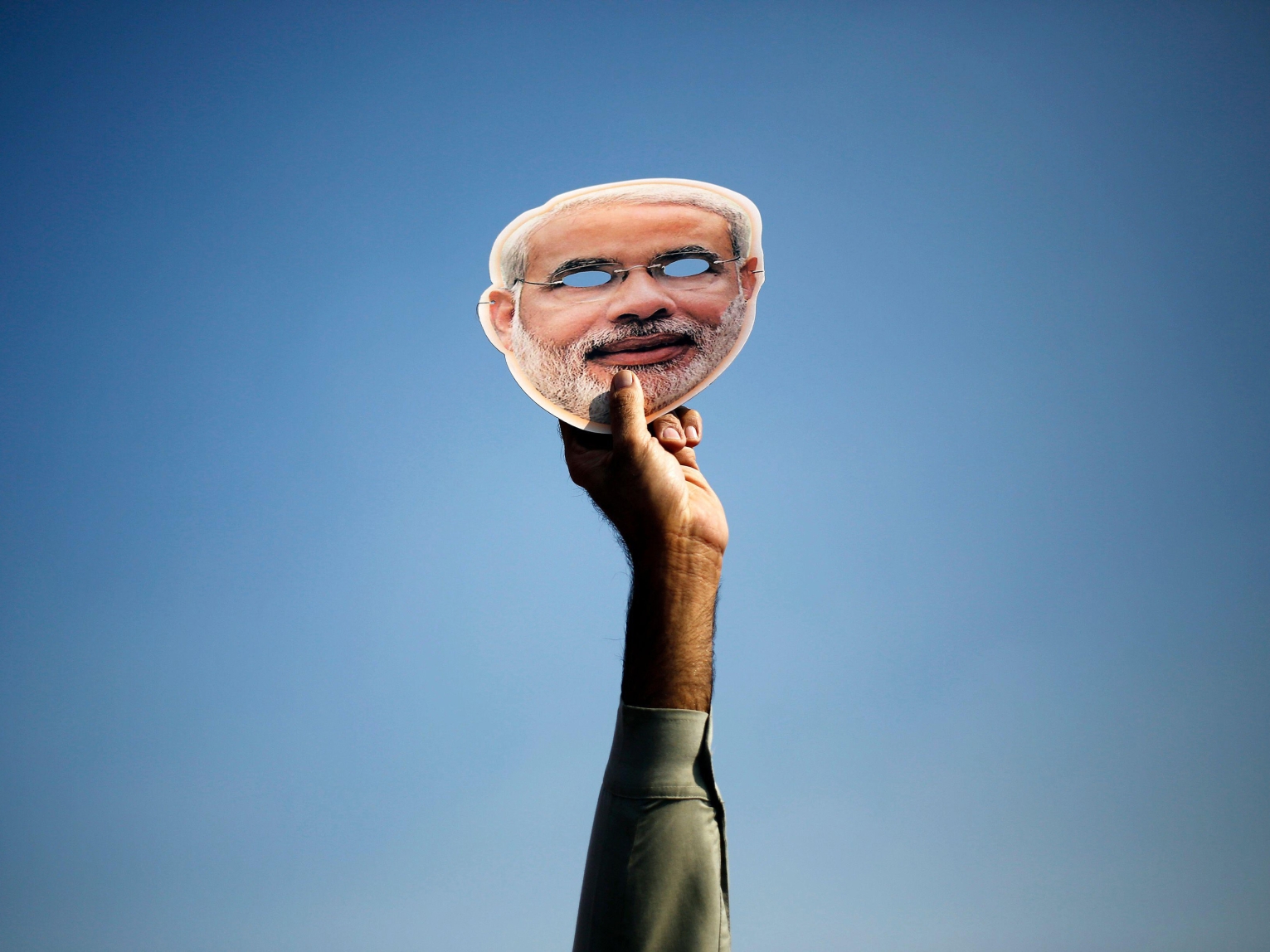A raised hand holds a mask depicting Indian Prime Minister Narendra Modi.