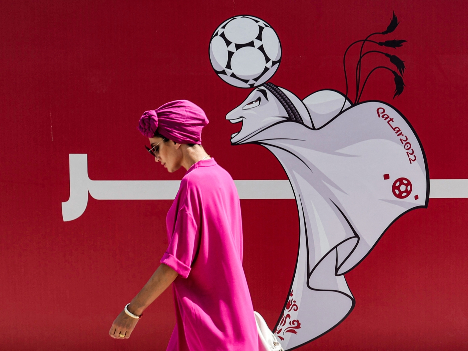 A woman walks past a construction site fence showing an illustration of the Qatar 2022 FIFA World Cup mascot "La'eeb" in West Bay in Qatar's capital Doha on October 13, 2022.