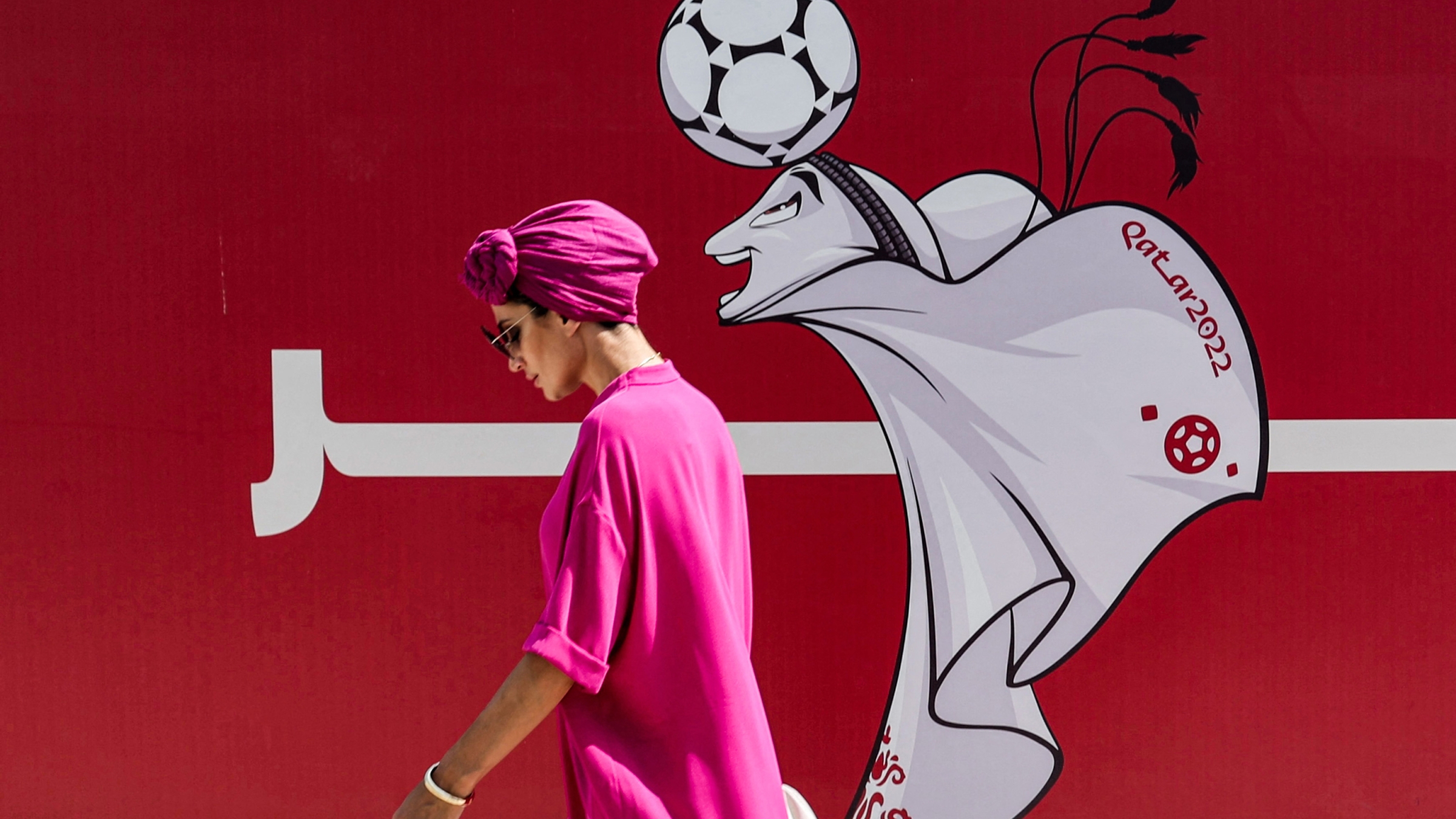 A woman walks past a construction site fence showing an illustration of the Qatar 2022 FIFA World Cup mascot "La'eeb" in West Bay in Qatar's capital Doha on October 13, 2022.